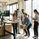 Diverse kantoormedewerkers leren ergonomische werkplektechnieken, monitorhoogte aanpassen en juist tillen in moderne werkruimte