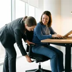 Ergonomie consultant past bureaustoel aan terwijl werknemer comfortabel zit aan verstelbaar bureau in moderne werkruimte