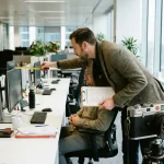 Ergonomie consultant meet monitorhoogte tijdens werkplek assessment met werknemer aan bureau in moderne kantooromgeving