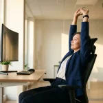 Kantoormedewerker strekt armen boven hoofd aan ergonomisch bureau met verstelbare monitor in modern kantoor